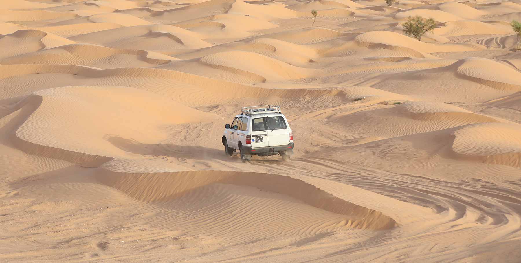 Jeep fährt durch Dünenlandschaft der Sahara