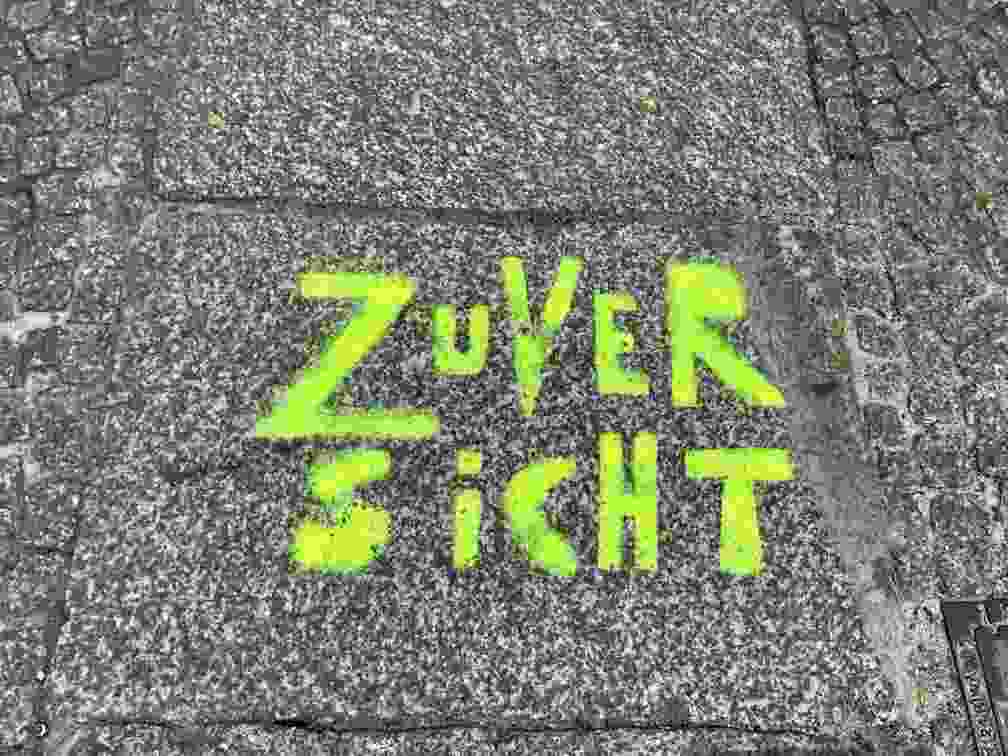 Auf dem Foto steht Zuversicht in Neonschrift auf einem Asphaltpflaster / Bürgersteig