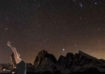 Frau in Yogapose unter einem Sternenhimmel in südlicher Hemisphäre, im HIntergrund einer Bergkette