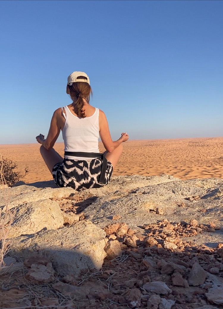 Frau sitzt auf einem Berg in der Wüste und meditiert