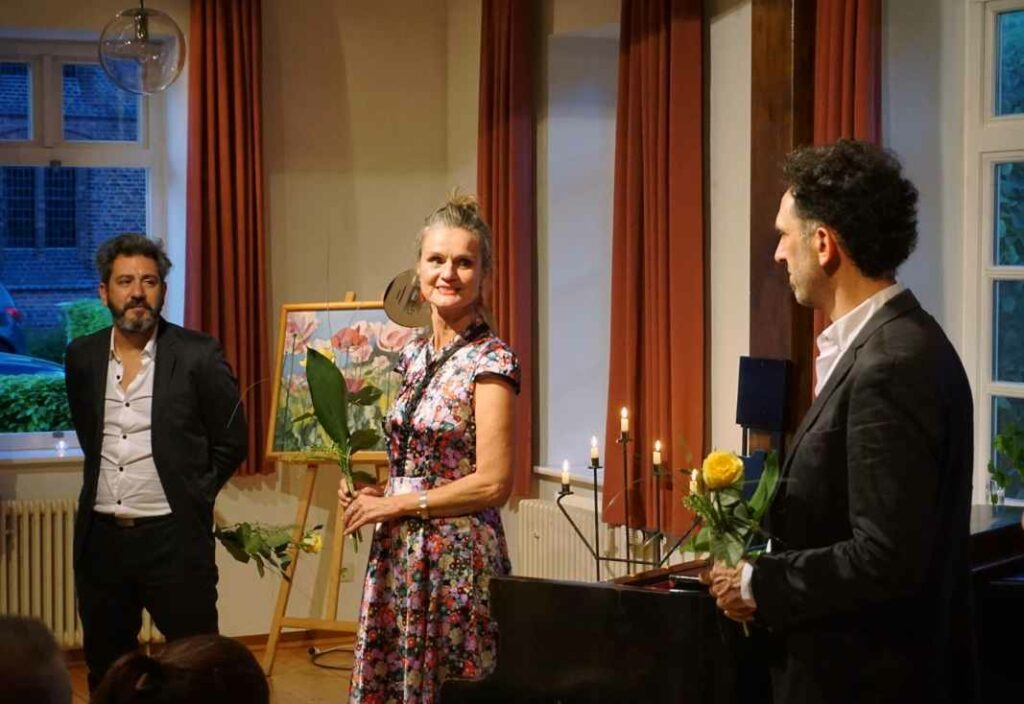 Frau mit zwei Musikern auf einer Bühne und Rose in der Hand