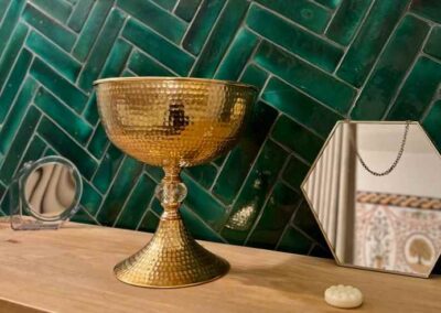 Goldene Amfore auf einem Sideboard, hinter grühner Fliesenwand auf Holzkommode