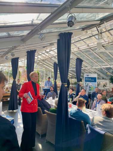 Frau in rotem Blazer vor Tischen mit Leuten