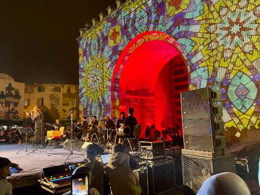 Lichtinstallation vor Stadttor mit Bühne und Orchester davor.