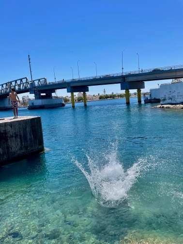 Ein Schwimmer ist gerade vor einer Brücke ins Wasser gesprungen, Aufprall und Wasserspritzer im Bild