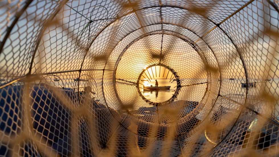 Ein Fischerboot im Sonnenuntergang auf dem Meer, durch ein Fischernetz fotografiert.